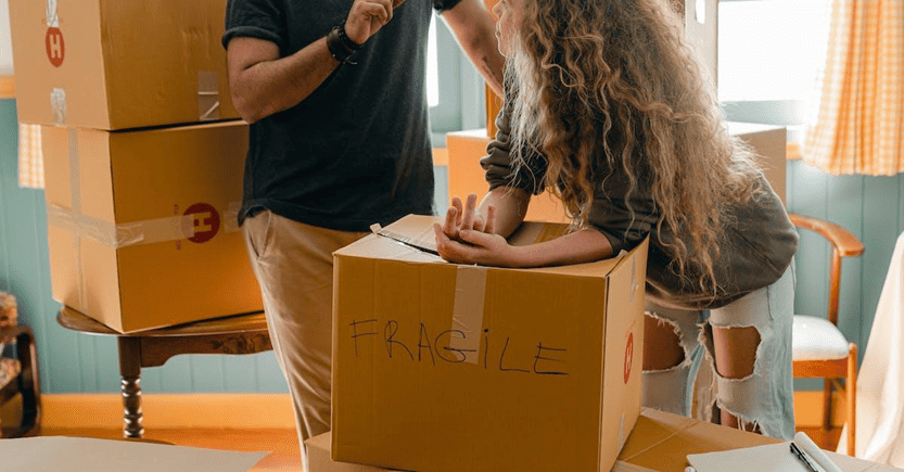 People organizing fragile items in moving boxes | eFinancialModels Couple discussing fragile box contents during a move