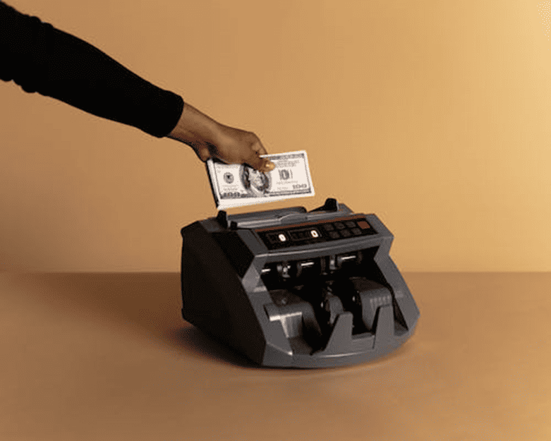 Cash Counting Machine with 0 Bill Insertion | eFinancialModels Hand placing a 0 bill into a currency counting machine for accurate cash handling.